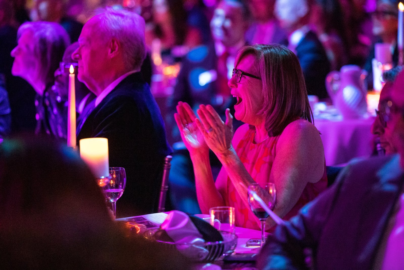 Woman in pink lighting clapping and smiling in delight.